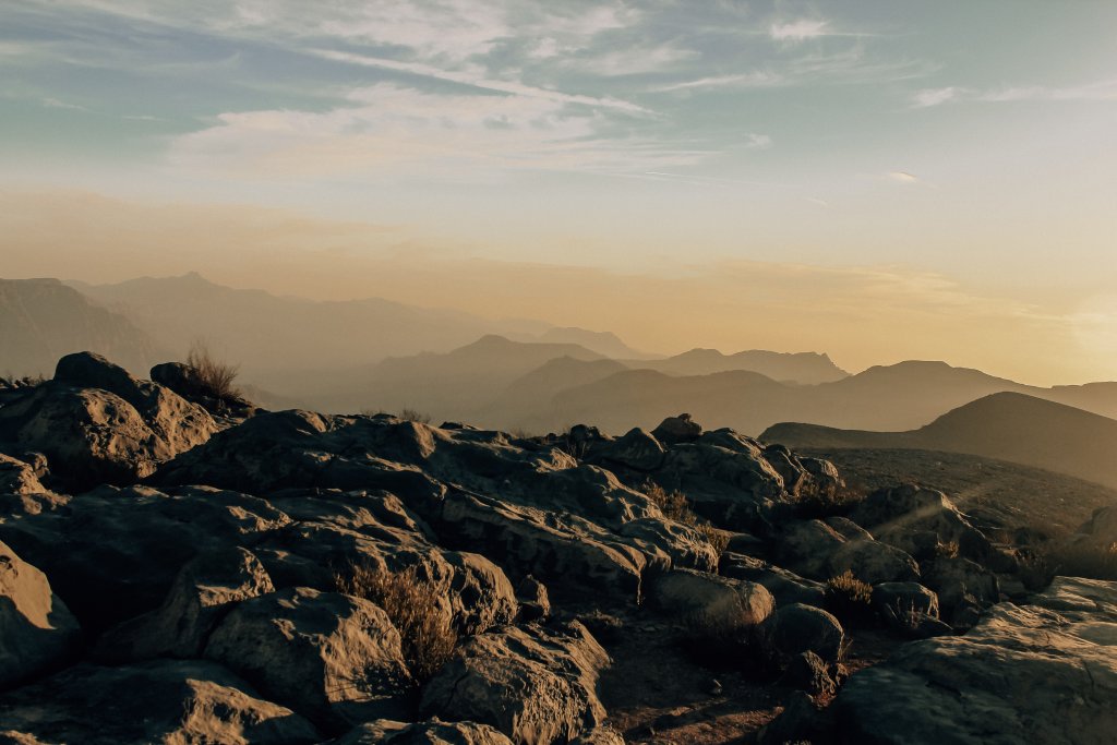 The rugged mountains of Oman in front of a orange and blue sunset sky.