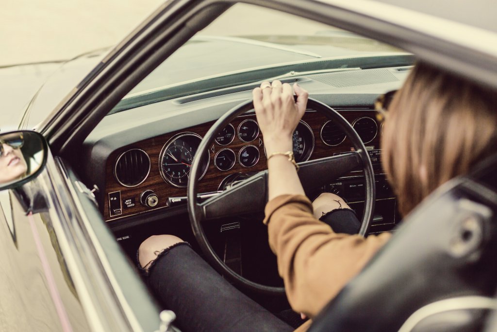 A girl in a brown shirt driving a car alone.