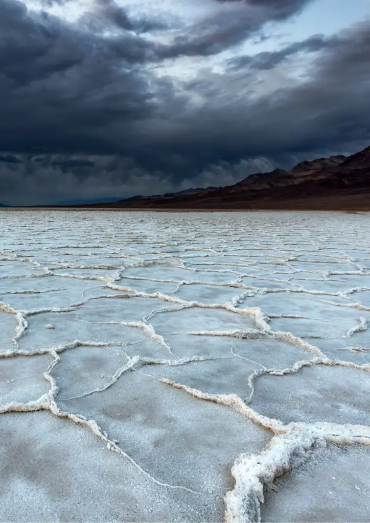 Badwater Basin salt floor, in front of tall mountains and cloudy skies.