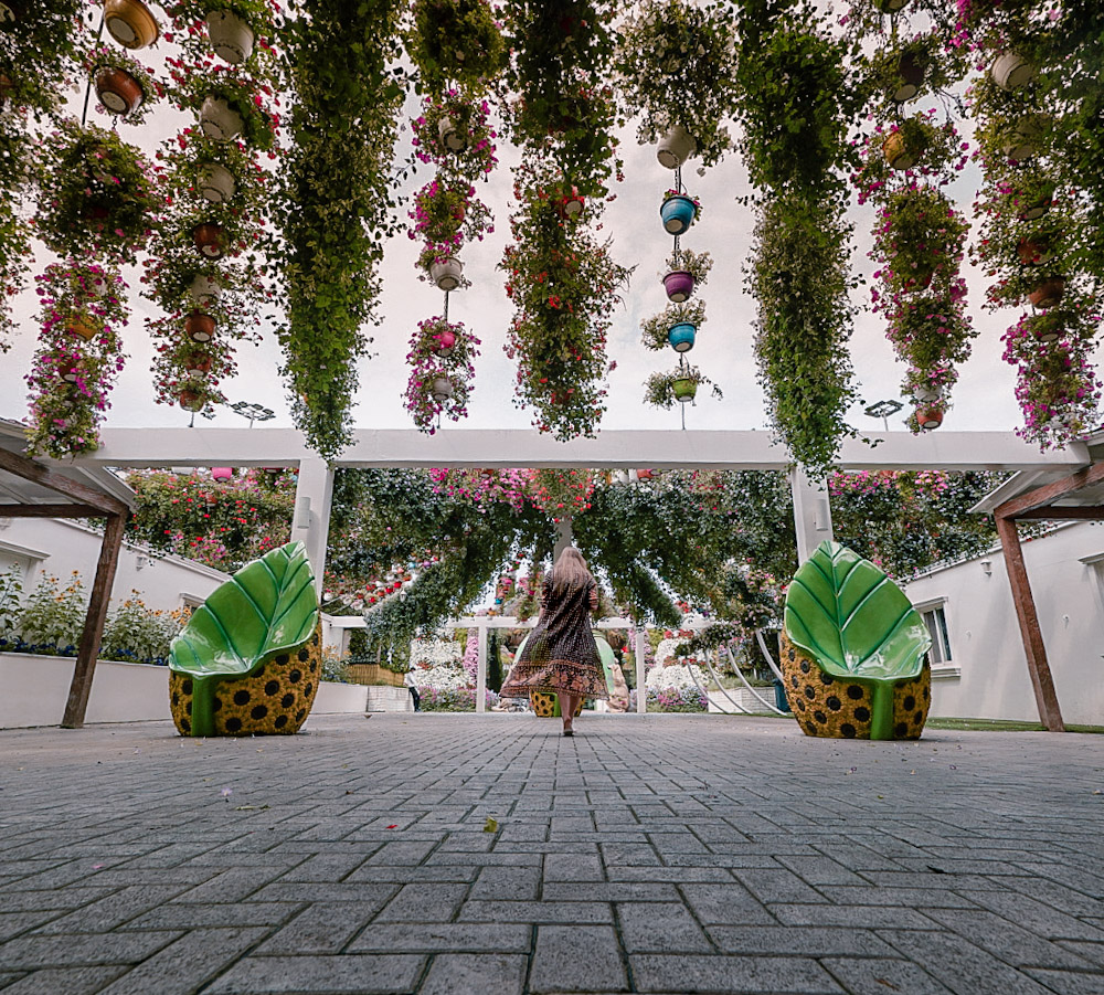 Monica walking under green foliage at the Dubai Miracle Garden.