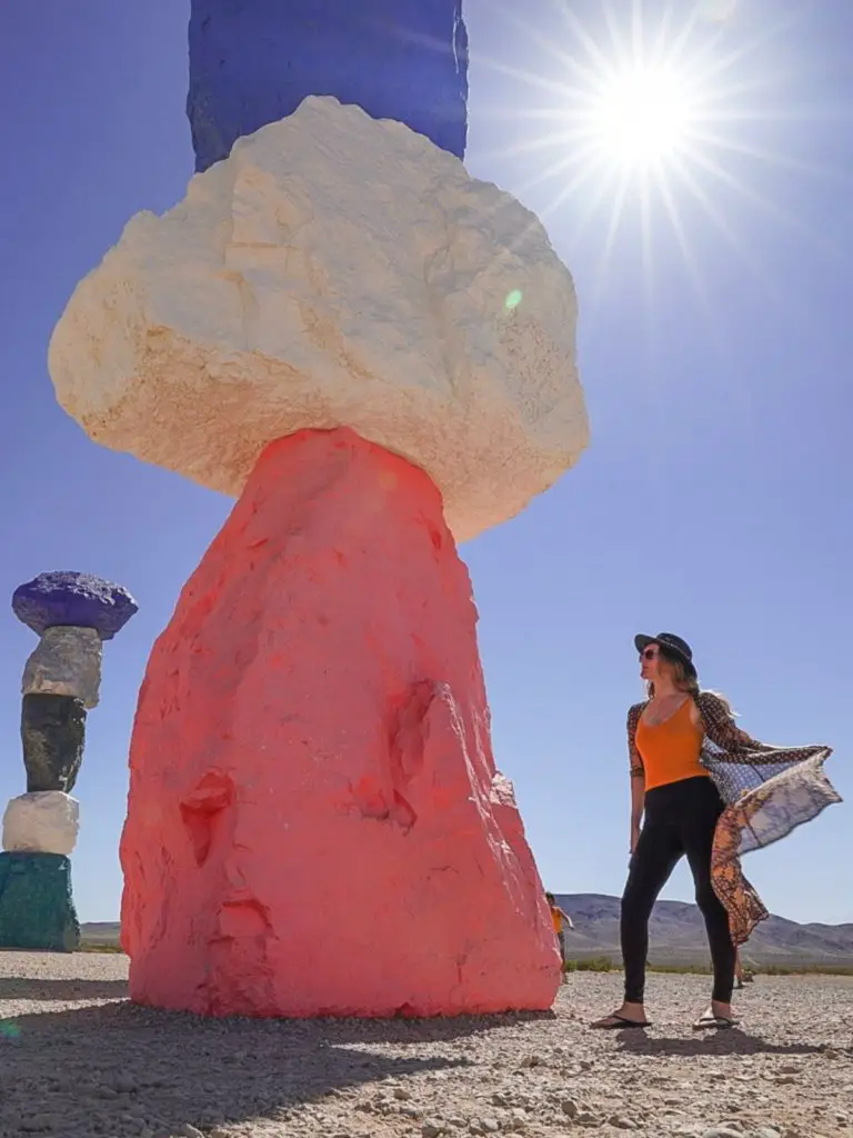Monica standing next to a giant pink and rainbow colored rock sculpture under the bright Nevada sun.