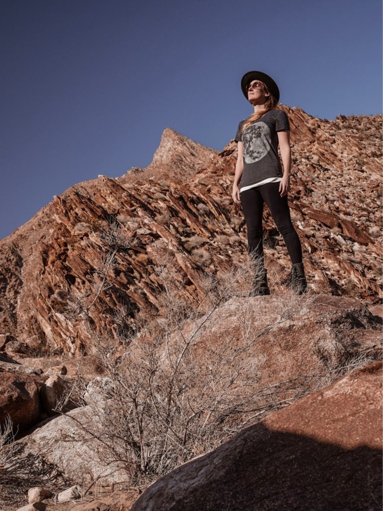 Monica Hiking the Anza Borrego Palm Canyon Trail with a red rock backdrop and blue skies.