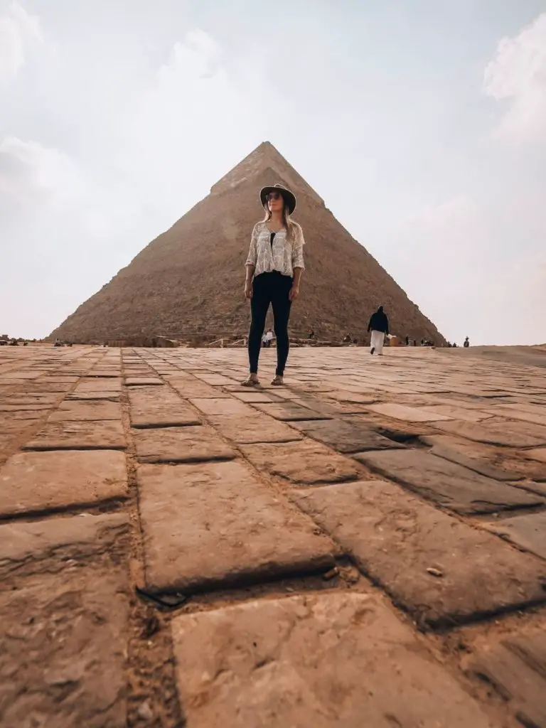 Standing in front of an ancient pyramid wearing long pants and long sleeves -  an Egypt packing list for women.