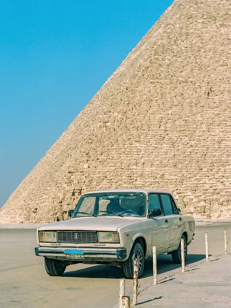 A car with an Arabic license plate in front of the pyramids.