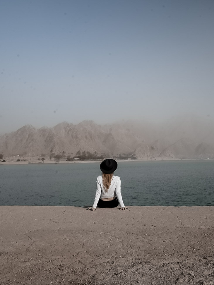 Monica sitting in front of the blue water at Lake Cahuilla Veterans Regional Park, one of the best day trips from Palm Springs!