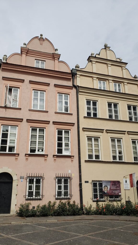 Two buildings, yellow nad pink, with famous Amsterdam-style roofs.