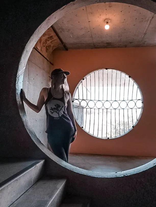 Monica Visiting Arcosanti, standing in a pink room with circular windows.