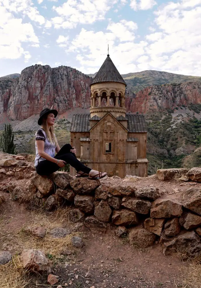 Monica sitting on the rock wall, looking at Noravank Monastery, one of The Best Places to Visit in Armenia.