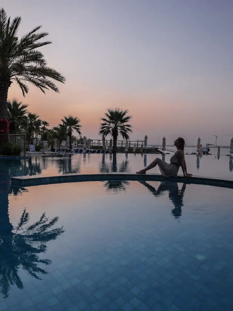 Monica sitting on the edge of the infinity pool at sunrise - one of the best Places to Visit in Ras Al Khaimah.
