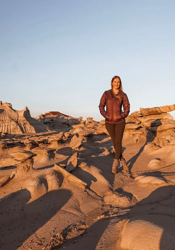 Monica exploring the Bisti Badlands / De Na Zin Wilderness, standing on a rock at sunset.