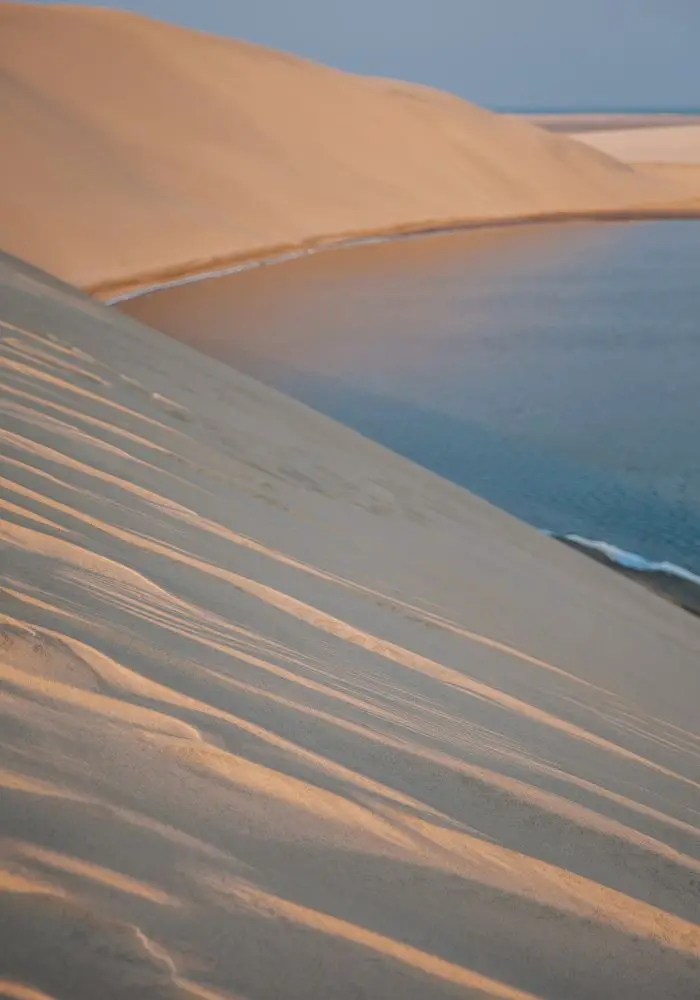 The tan sand dunes against the blue sea, a must see in Doha.