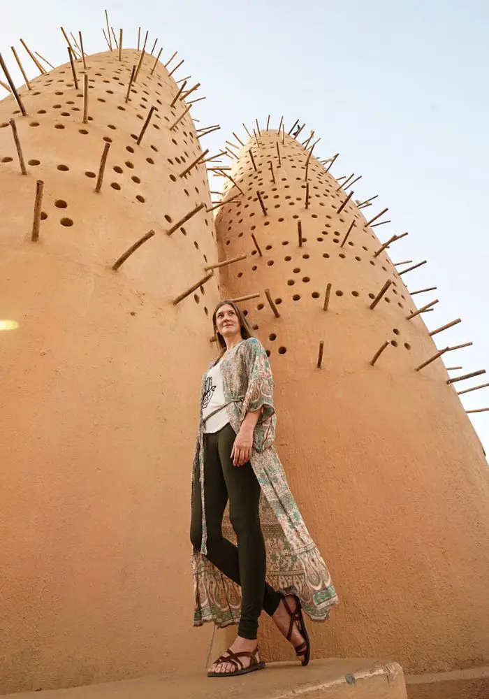 Monica standing in front of the tan colored Pigeon Towers, a necessary stop on A One Day in Doha Itinerary.