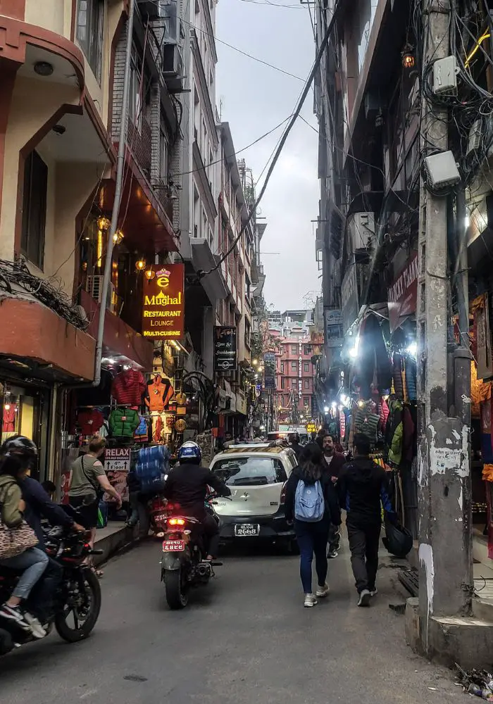 The crowded streets of Thamel with cars and pedestrians and scooters on a skinny street - one of the essential Things To Know Before Visiting Nepal.