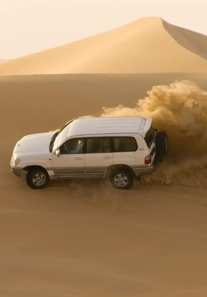 A white car driving on the sand dunes - one of the best Doha day trips and tours.