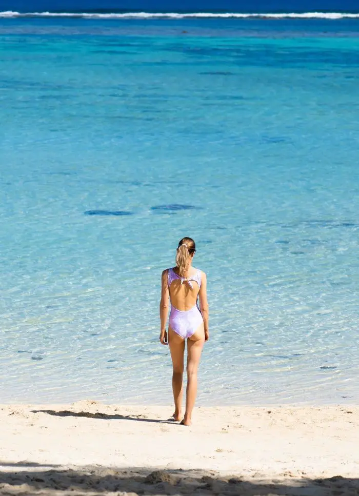 Girl in a white bathing suit near the blue water that you'll see during Cook Islands travel.