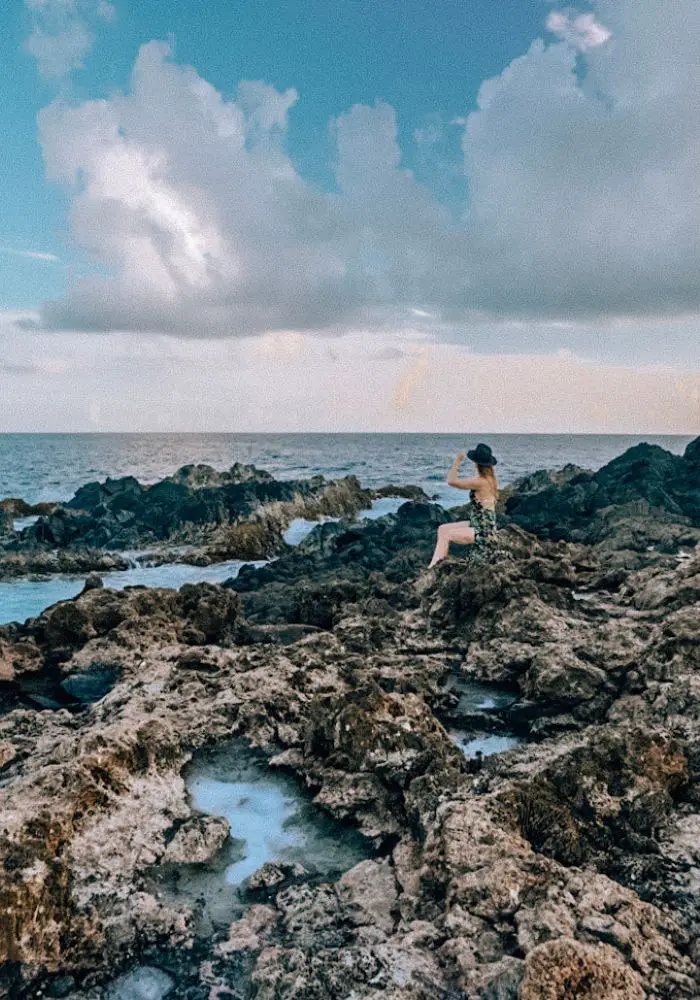 Monica on the rocky shore of Aruba, under cloudy skies.