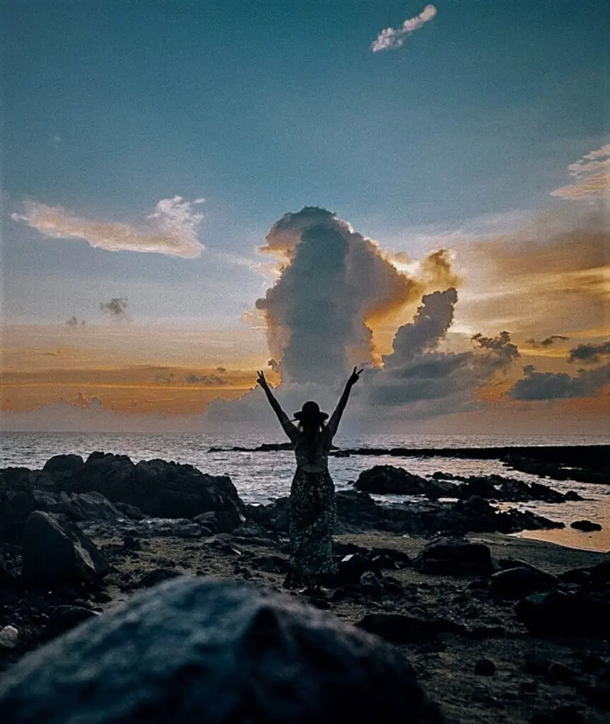 Monica with her hands raised, celebrating the beautiful sunrise in Aruba.