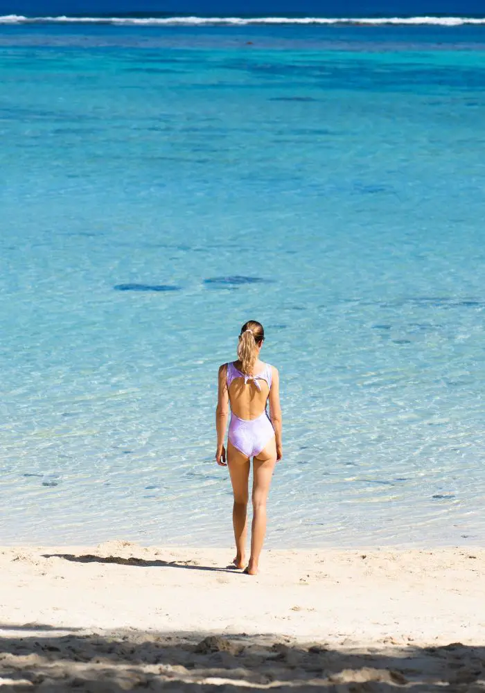 Girl in a white bathing suit on the white sand beach on the Cook Islands.  One interestingCook Islands fact, there are 15 islands here.