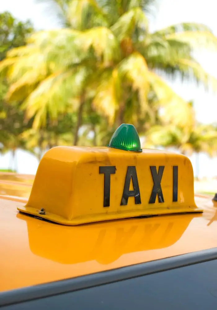 A yellow taxi in Aruba in front of green palm trees, a great mode of transportation.