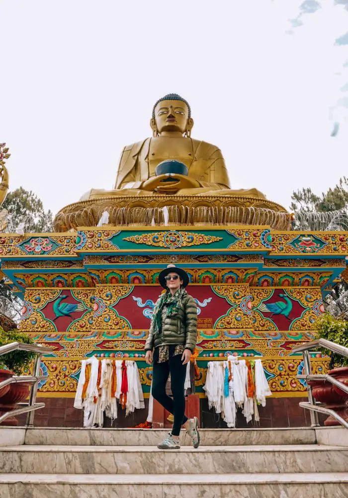 Monica in a green jacket standing in front of a golden Buddha statue in Spring, one of the best season in Nepal for travelers.