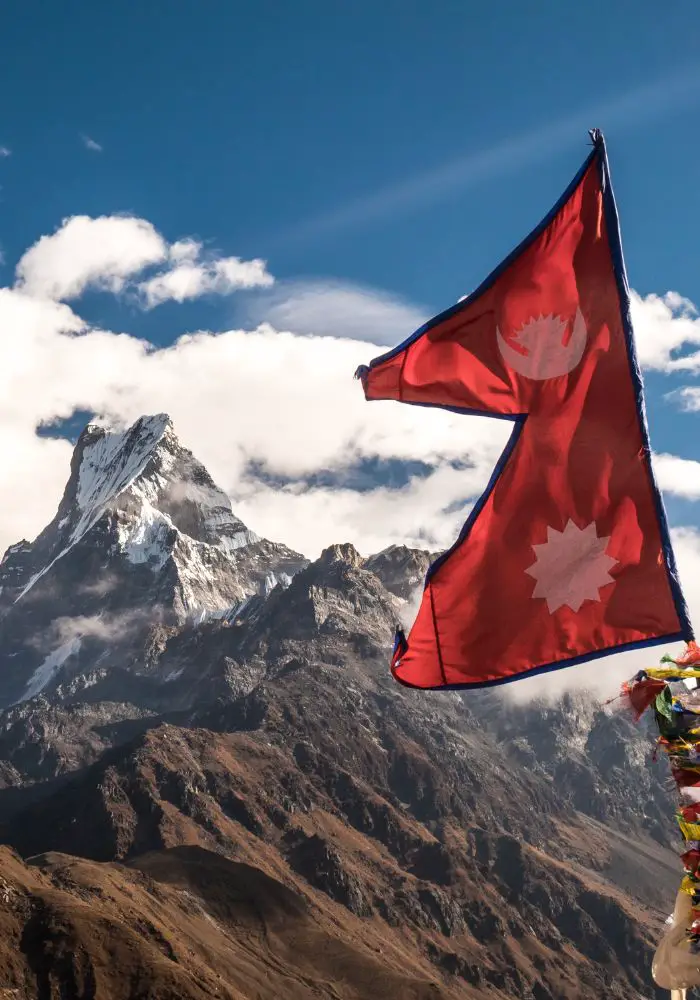 A bright red Nepal flag billowing in the wind in front of the mountains.