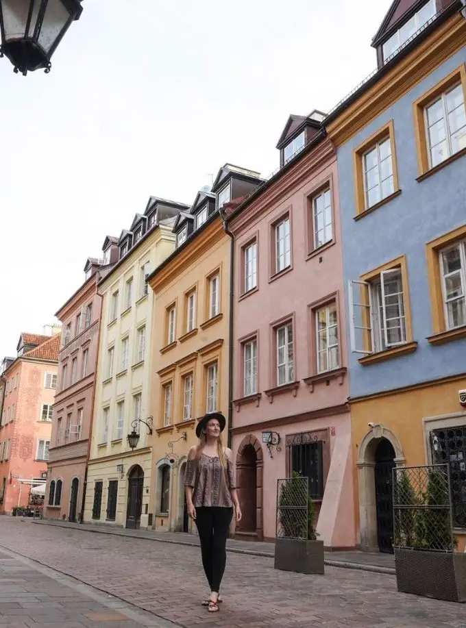 Monica walking between the pastel architecture on Old Town Warsaw's streets.