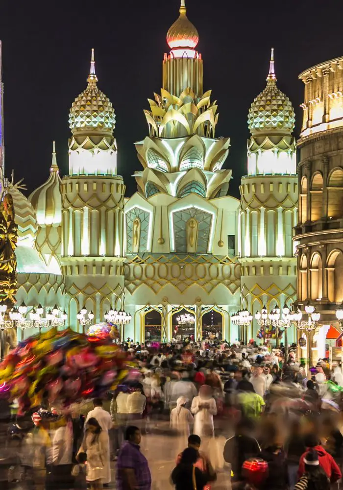 The lit up Global Village with a swarm of people moving around in a crowd.
