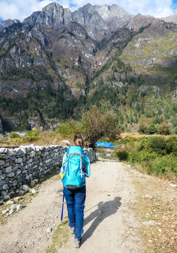Girl trekking toward a mountain in Nepal while wearing a blue backpack and trekking poles - two items on your Nepal trekking packing list.