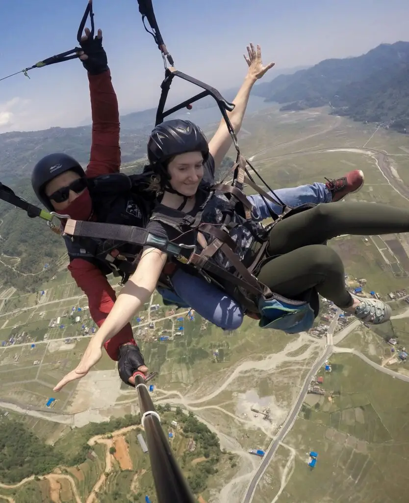 Monica and Deepak paragliding in Pokhara, Nepal, high above the green valley below.