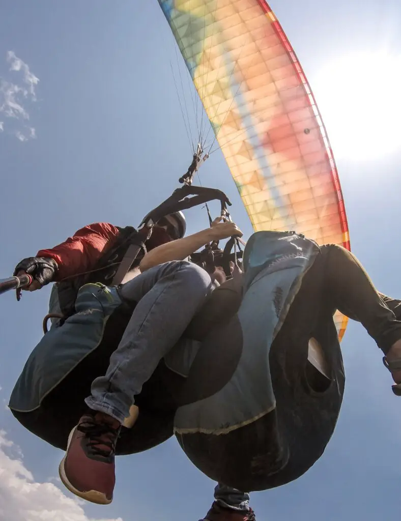Monica and Deepak paragliding in Pokhara, Nepal, underneath a rainbow colored parachute.