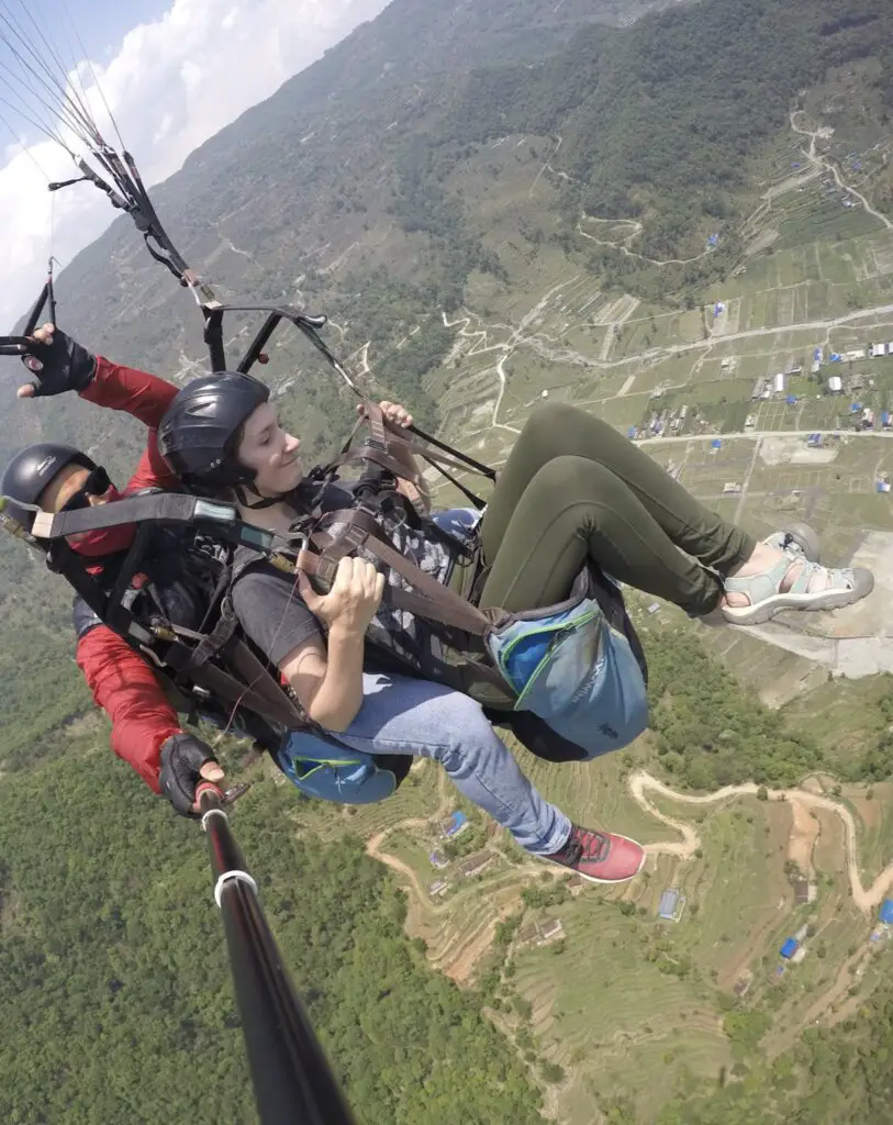 Monica in green pants and Deepak in a red coat, paragliding in Pokhara, Nepal.