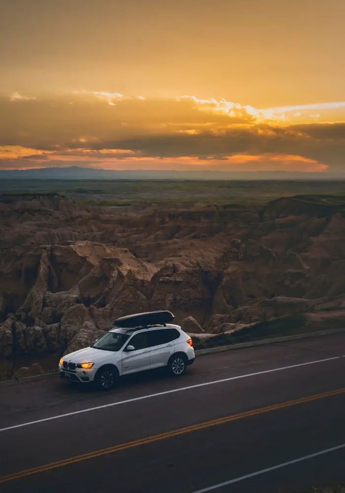 A beautiful sunset above a white car on a road trip alone.
