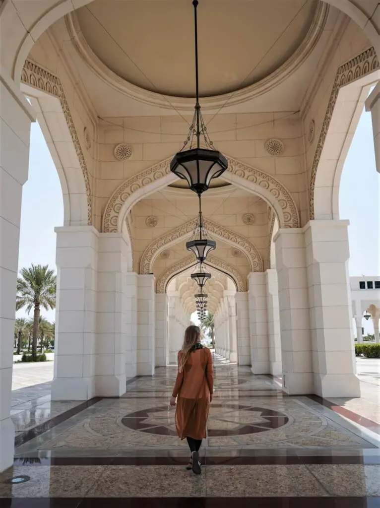 Monica walking down an outdoor pathway surrounded by white columns.