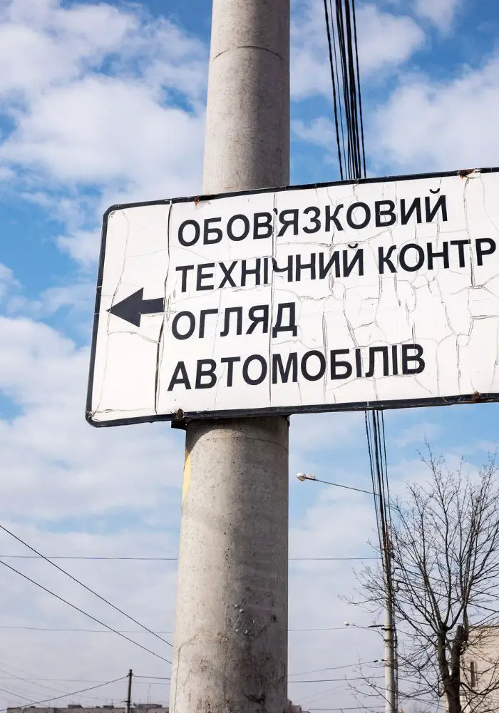 A white road sign with Cyrillic lettering in front of a cloudy sky.