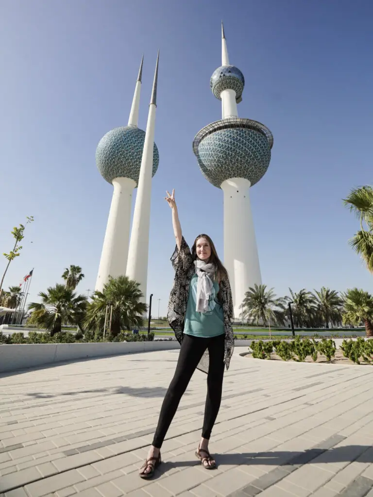 Monica standing tall in front of the Kuwait Towers, in front of a blue sky.