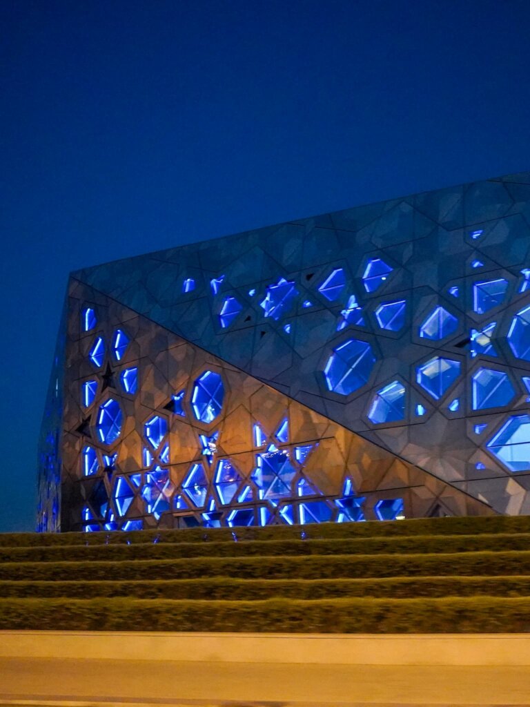 The Sheikh Jaber Al-Ahmad Cultural Centre lit up at night, with blue glowing lights.