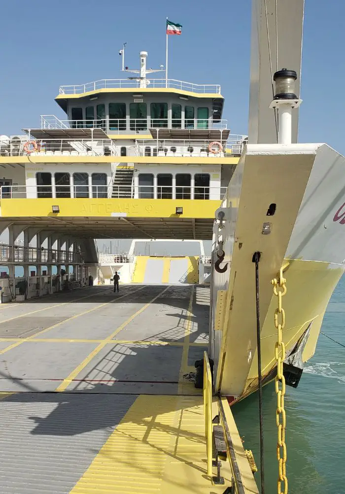 The yellow and white ferry to Failaka Island in Kuwait on blue water on a sunny day.