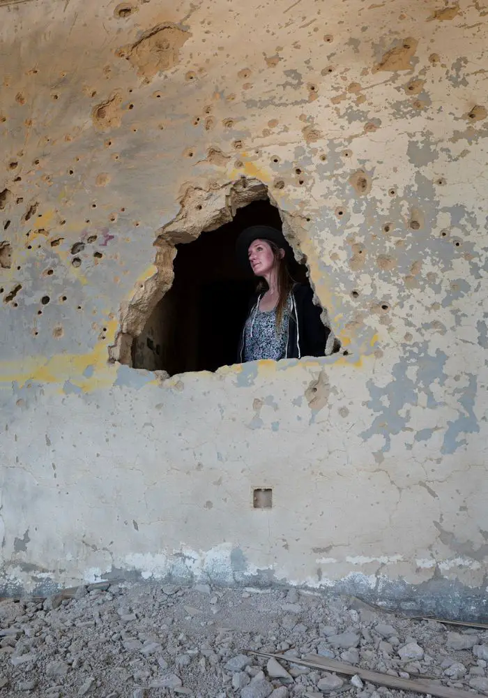 Monica next to bullet holes and destruction inside the National Bank of Kuwait on a Failaka Island day trip.