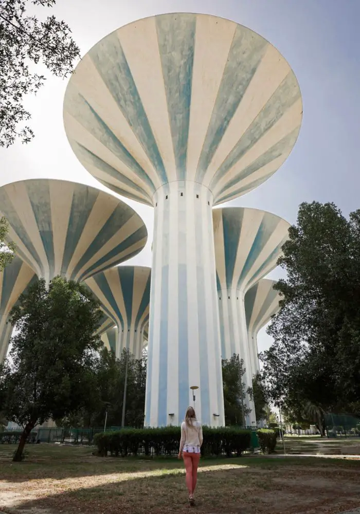 Monica traveling as a solo female in Kuwait, in front of blue and white striped water towers.