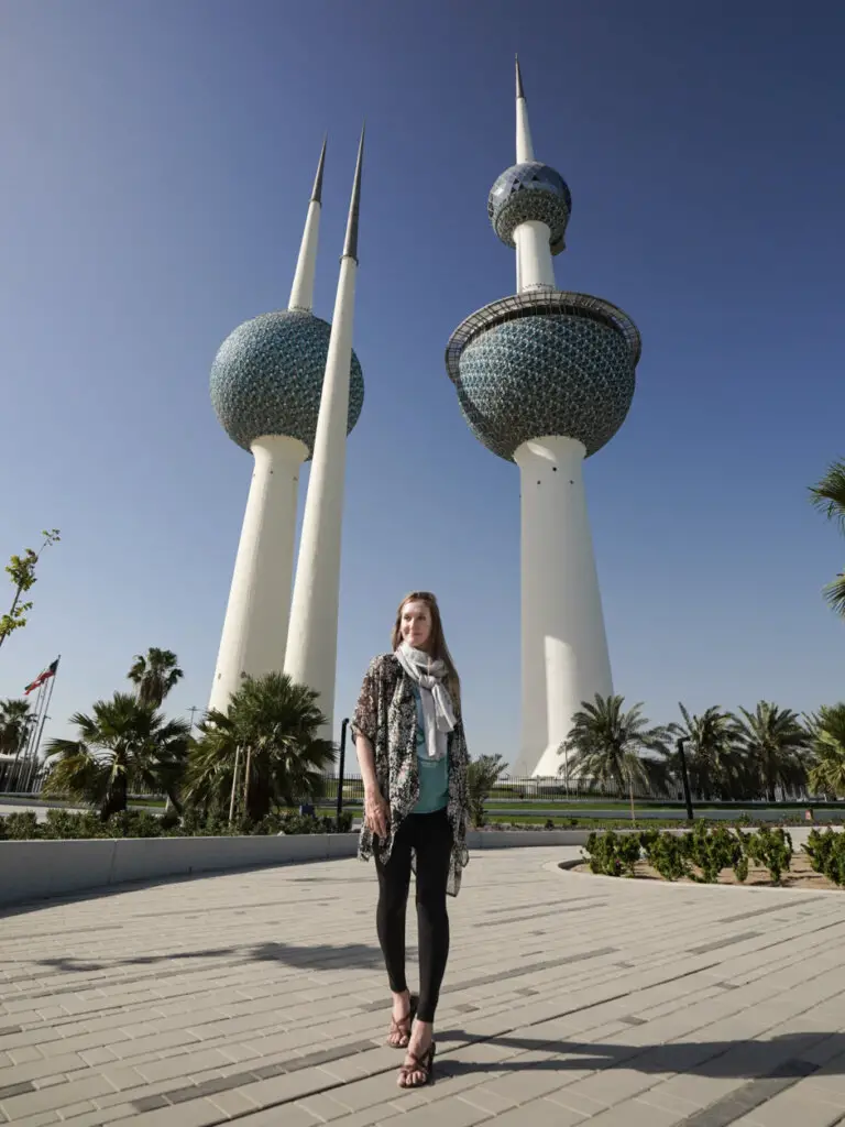 Monica walking in front of the 600 foot tall Kuwait Towers, wearing a long flowy shirt and scarf.