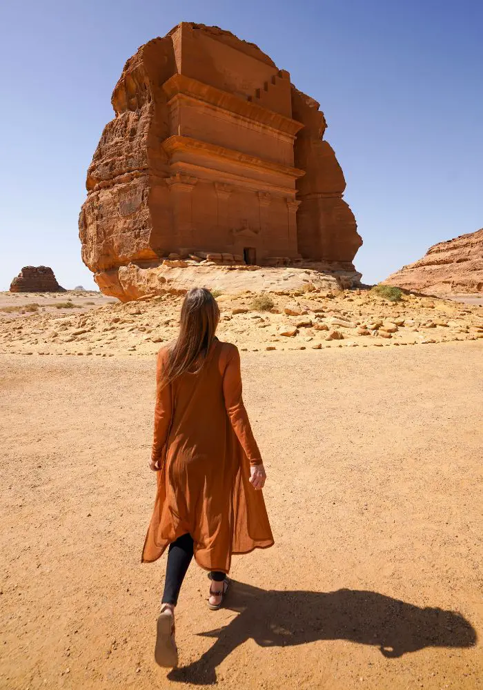 Monica on a sunny day, walking towards the main tomb at Hegra, one of the best things to do in AlUla Saudi Arabia.