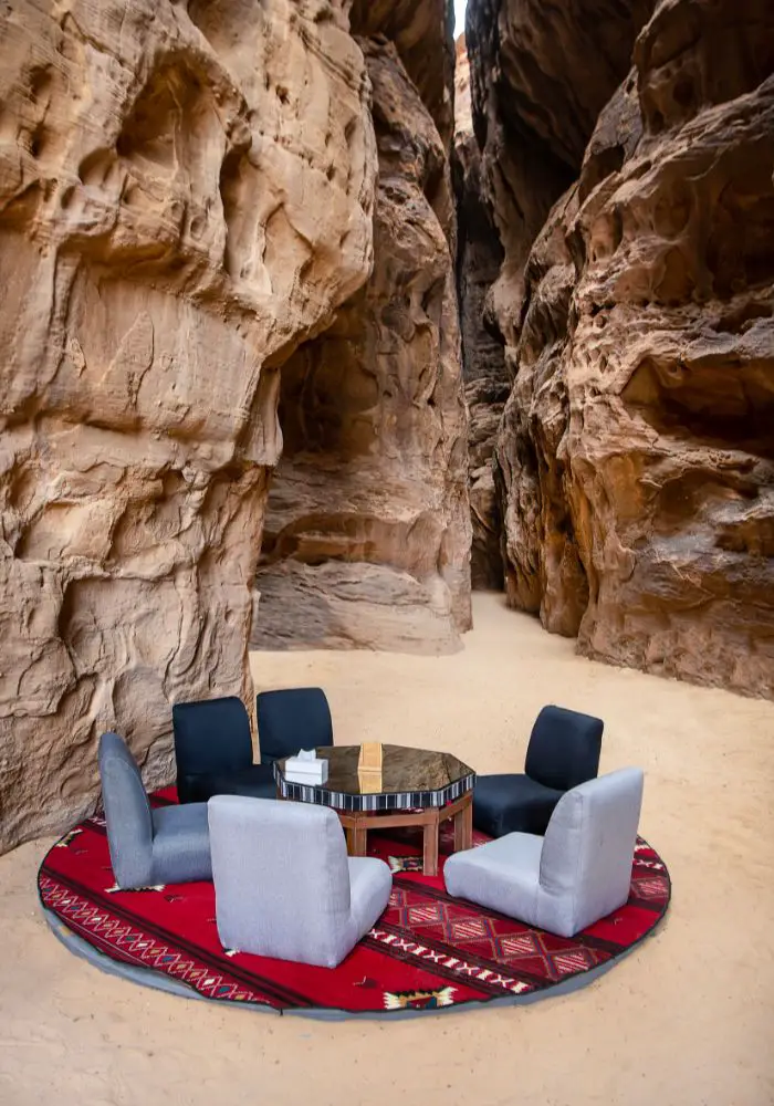 A table and chairs on the other side of the rocks on a red carpet.