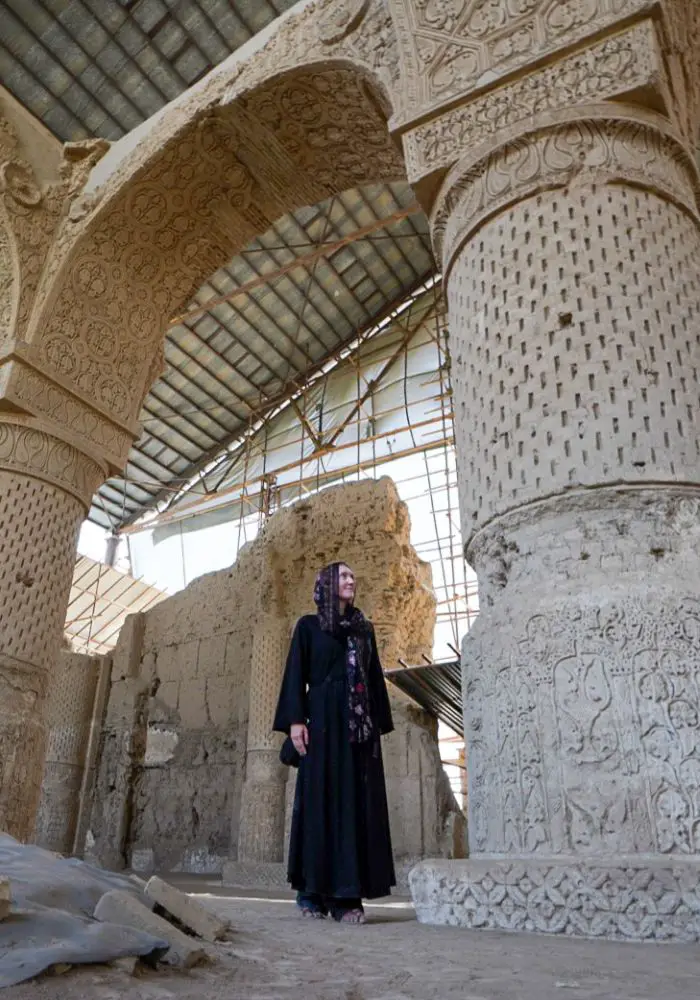 Monica wearing a black abaya, looking closely at the intricate carvings on a column at Balkh.