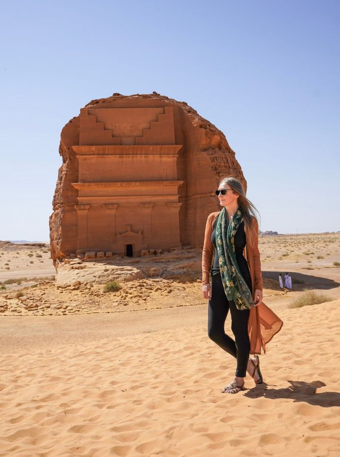 Monica, an American traveling in Saudi Arabia, posing in front of AlUla's famous orange tombs.