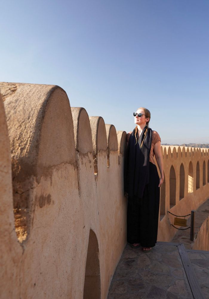 Monica wearing black and tan clothing, gazing out through sunglasses from the top of Nizwa Fort, one of the best places to see in Oman.