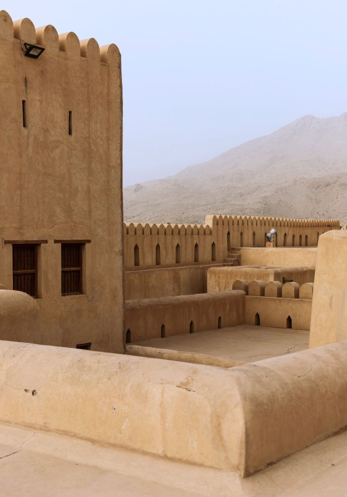 The sand colored architecture of the Nizwa Fort on a foggy day.