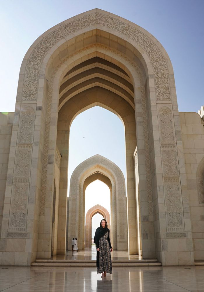 Monica traveling as a woman in Oman, walking under the arches at the Grand Mosque.