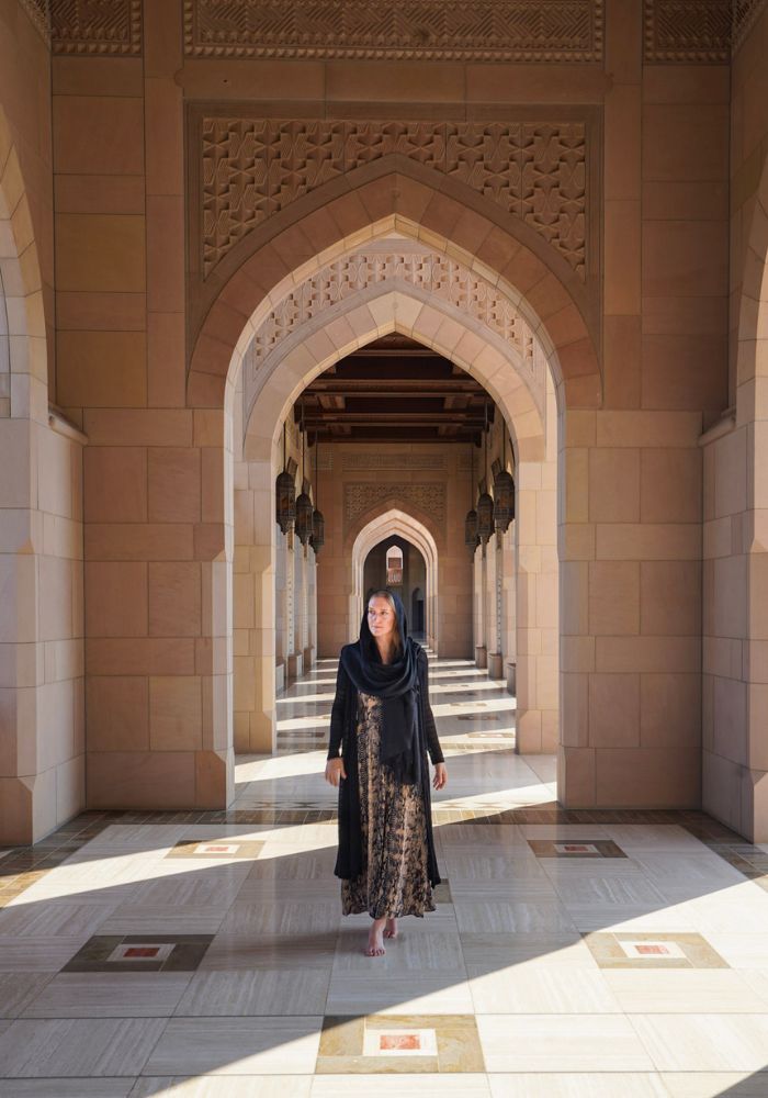 Monica, a woman traveling Oman wearing a long dress and black scarf in a mosque.