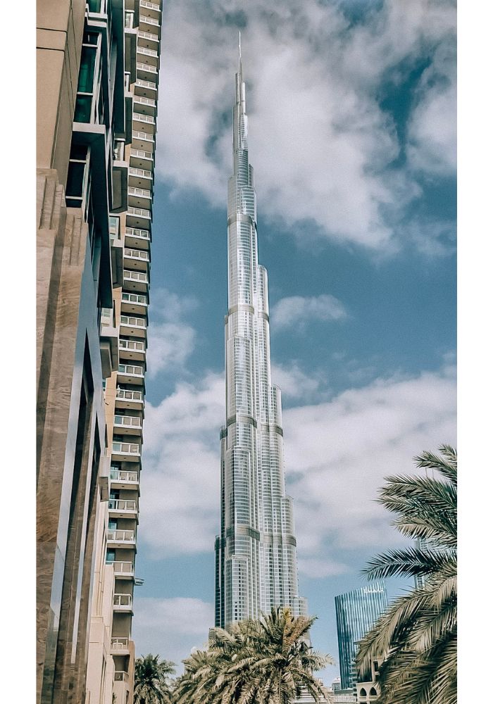 The tall silver Burj Khalifa, towering in front of the blue cloud-covered sky.